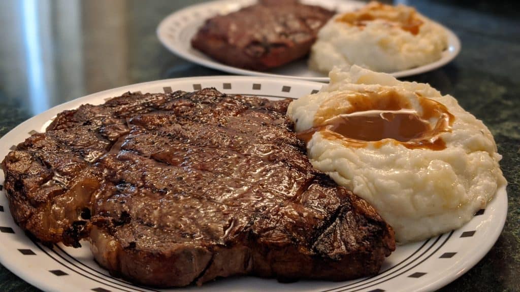 photo of a ribeye steak with mashed potatoes and gravy after grilling frozen steaks
